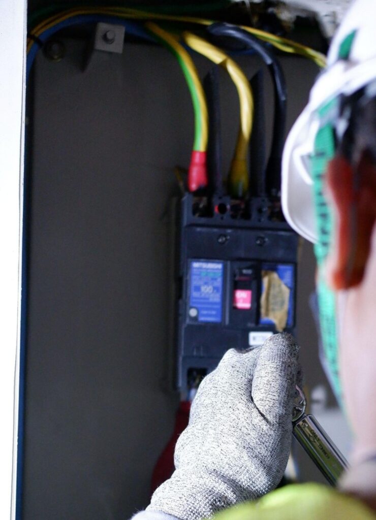 Electrician in protective gear servicing an industrial breaker panel in Boise, ID.